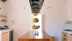 Une cuisine moderne avec une table en bois, des paniers à fruits suspendus et une vue sur l’extérieur.