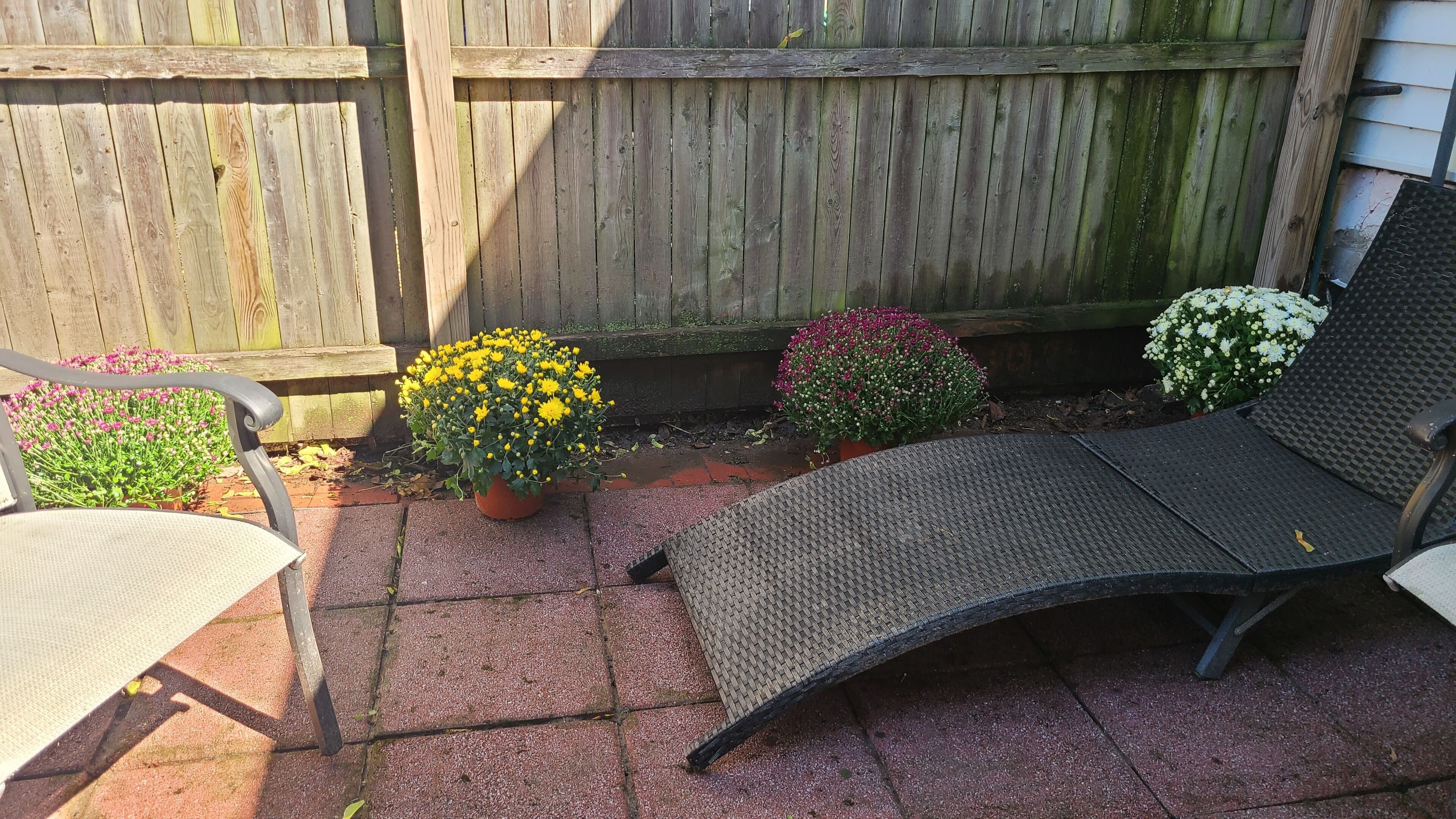 A patio with a metal chair, a cushioned chair, and potted plants.