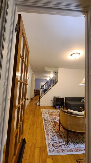 A hallway with wooden flooring, a patterned rug, a sofa, and a staircase with a railing. - Humble Abode (Ardmore)