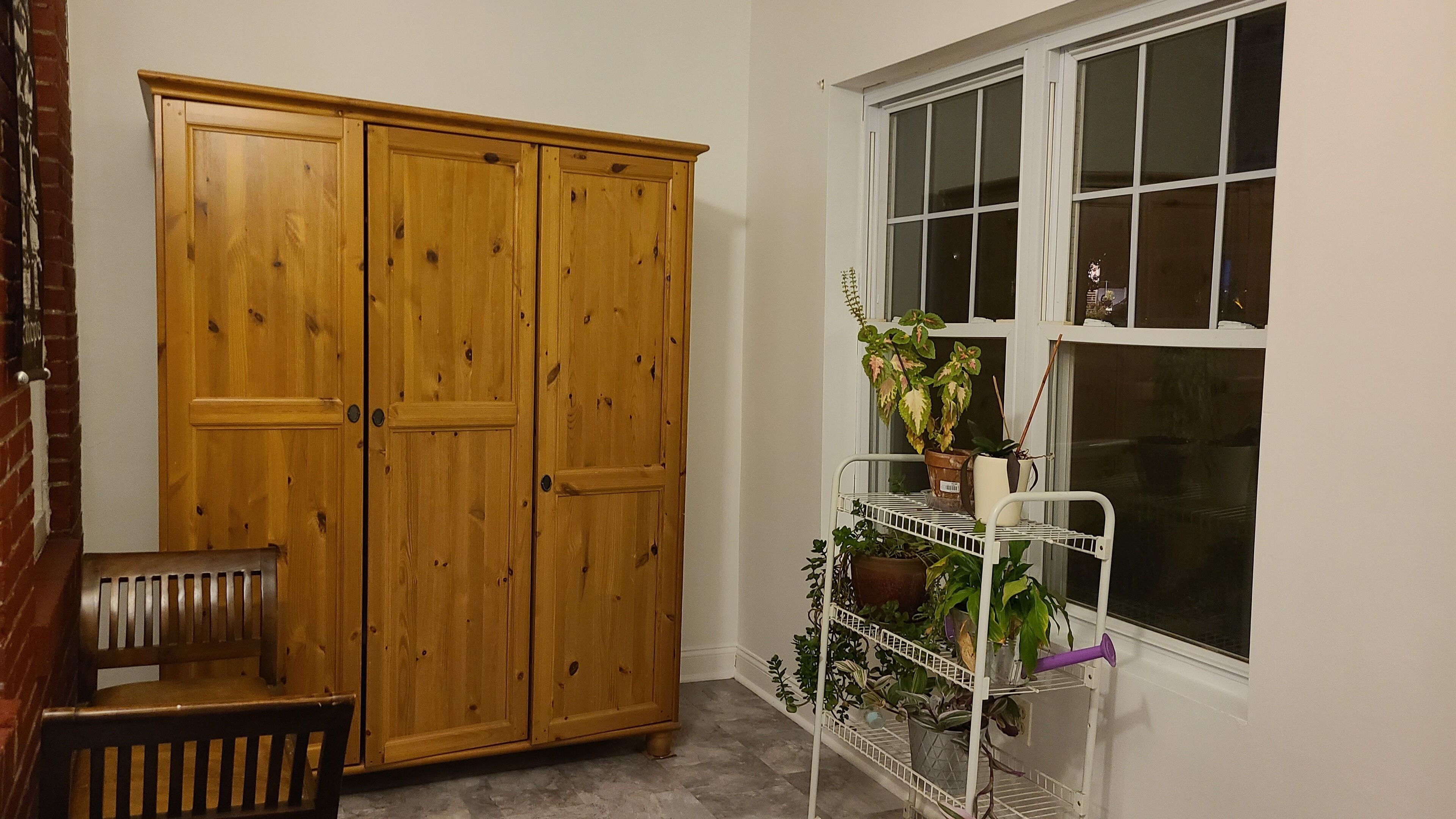 A room with a wooden wardrobe, a bench, and a window with a plant shelf.
