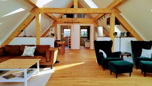 A spacious loft with high ceilings and exposed wooden beams. It features a cozy seating area with a couch and chairs, a dining table, and a kitchen area with a refrigerator and sink. - "Basalt barn Westerwald" - close to nature & unique (Stahlhofen)