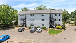 A multi-story apartment building with a parking lot, two staircases, and a small lawn area.