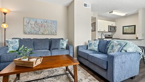 A living room with two blue sofas, a wooden coffee table, and a painting on the wall.