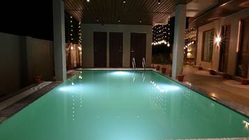 A swimming pool with a clear water surface, surrounded by potted plants and a wooden ceiling structure.