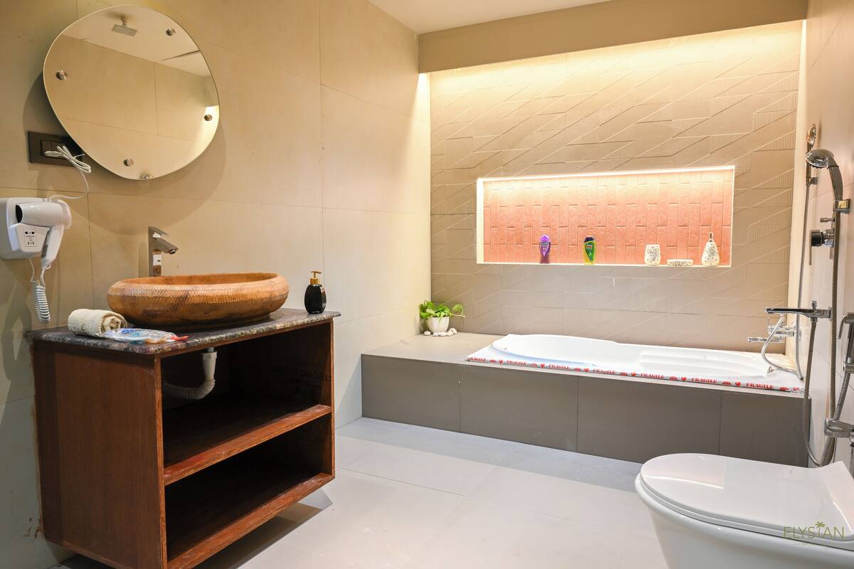 Un baño moderno con tocador de madera, un espejo redondo, una bañera grande y un inodoro.