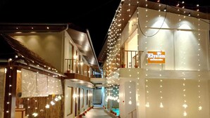 A hotel corridor with a green carpet, potted plants, and string lights. - The Elysian Boutique Stays (Port Blair)