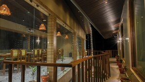 A covered outdoor seating area with wooden chairs and tables, potted plants, and string lights. - The Elysian Boutique Stays (Port Blair)