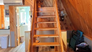 Una escalera de madera conduce a una zona superior con una cocina visible al fondo.