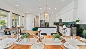 Une cuisine moderne avec des meubles blancs, un îlot central et un coin repas aménagé pour six personnes, avec une table en bois et six chaises.