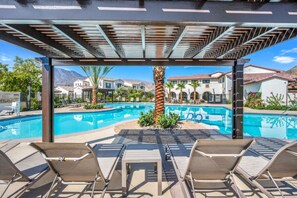 Ein Poolbereich mit Liegestühlen, einer Pergola und Blick auf Villen im Hintergrund.