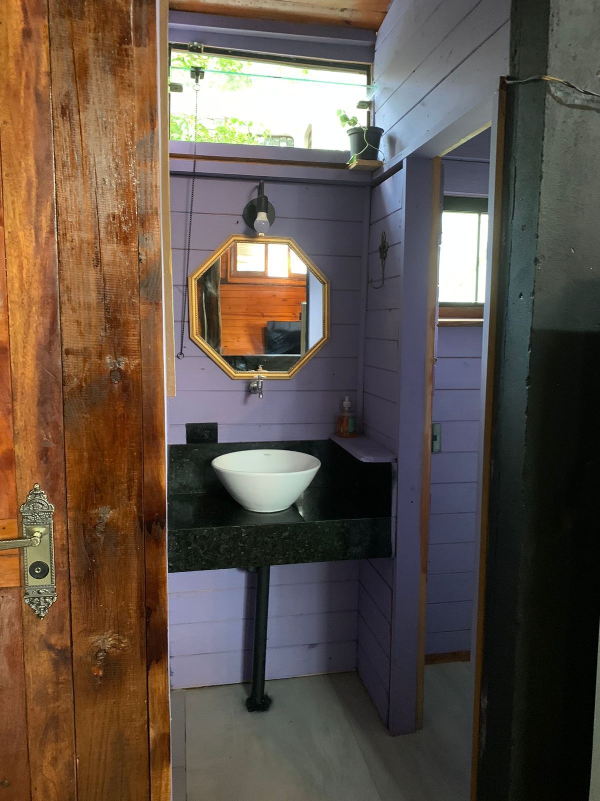 A bathroom with a wooden door, a white sink, a black countertop, and a hexagonal mirror.