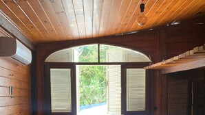 A wooden cabin bedroom with a bed, pillows, and a window with shutters. - URBAN CABIN - DOWNTOWN OF CASCAVEL. (Country Cascavel)