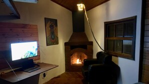 A cozy room with a fireplace, a desk with a laptop, a chair, and a television. - URBAN CABIN - DOWNTOWN OF CASCAVEL. (Country Cascavel)