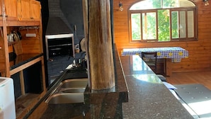 A kitchen with a central wooden pillar, a stone countertop, a sink, and a window with a view of greenery. - URBAN CABIN - DOWNTOWN OF CASCAVEL. (Country Cascavel)