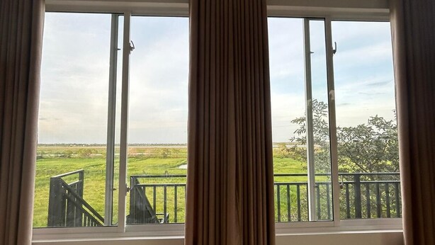A room with large windows overlooking a grassy field and a fence. - Neralu Garden Yala  (Tissamaharama)