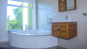 A bathroom with a freestanding bathtub, a wooden vanity, a mirror, and a window with a view of greenery. - Neralu Garden Yala  (Tissamaharama)