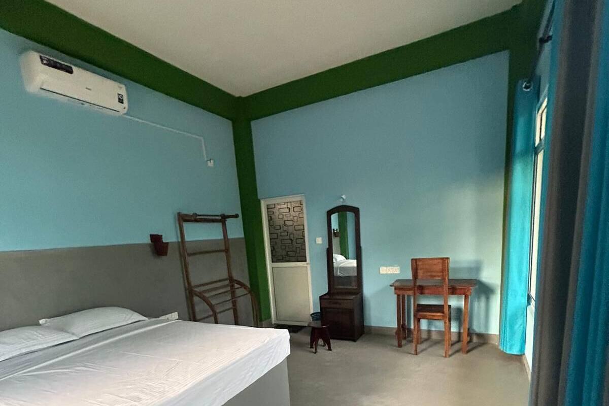 A hotel room with a bed, a desk, a chair, a mirror, and a window with curtains.