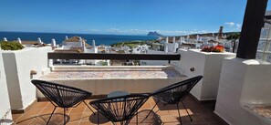 A terrace with two black chairs, a tiled table, and a view of the sea and buildings.