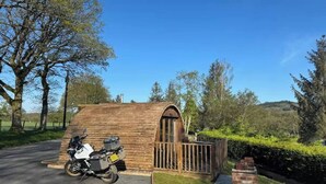 Una pequeña estructura de madera con techo inclinado, una motocicleta estacionada al frente y una chimenea de ladrillo.