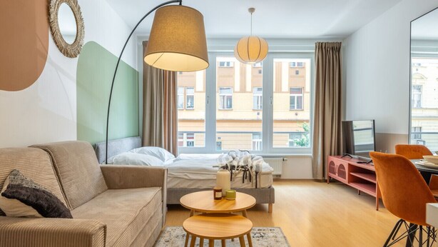 A modern hotel room with a sofa, a bed, a dining table, and a TV. - Designer Prague Studio in a Vibrant Neighborhood by EasyBNB Premium (Prague)