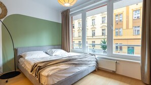 A bedroom with a bed, a radiator, a window with curtains, and a view of buildings outside. - Designer Prague Studio in a Vibrant Neighborhood by EasyBNB Premium (Prague)