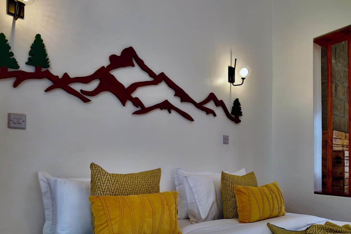 A bedroom with a bed, pillows, a wall-mounted light fixture, and a decorative wall piece.