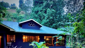 Una casa de dos pisos con fachada azul oscuro, ventanas amplias y un balcón.