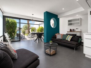A modern living room with a sofa, a dining area, and a kitchen.