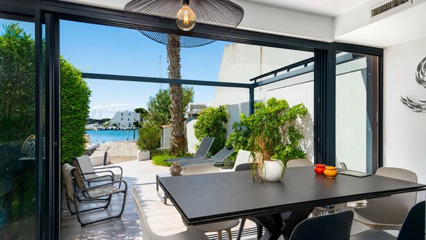 Un área de comedor exterior moderna con una mesa y sillas, una planta en maceta y vistas a una piscina y edificios.