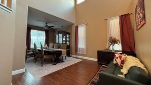 A spacious living room with hardwood flooring, a dining area with a table and chairs, and a large window with curtains. - 4-bedroom pool house in Fresno, hub for all California destinations &attractions (Fresno)