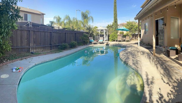 A backyard with a swimming pool, a covered patio area, and a wooden fence. - 4-bedroom pool house in Fresno, hub for all California destinations &attractions (Fresno)