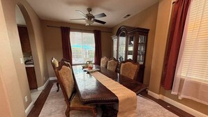 A dining room with a long wooden table, six chairs, a chandelier, and a ceiling fan. - 4-bedroom pool house in Fresno, hub for all California destinations &attractions (Fresno)