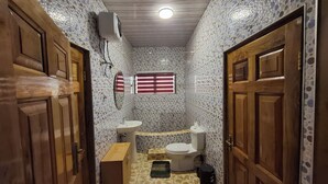 Ein schmales Badezimmer mit gefliestem Boden, Toilette, Waschbecken und Spiegel.