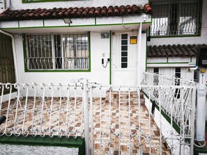 Un bâtiment avec un toit recouvert de tuiles, une porte blanche dotée d’une fenêtre et un portail en métal.