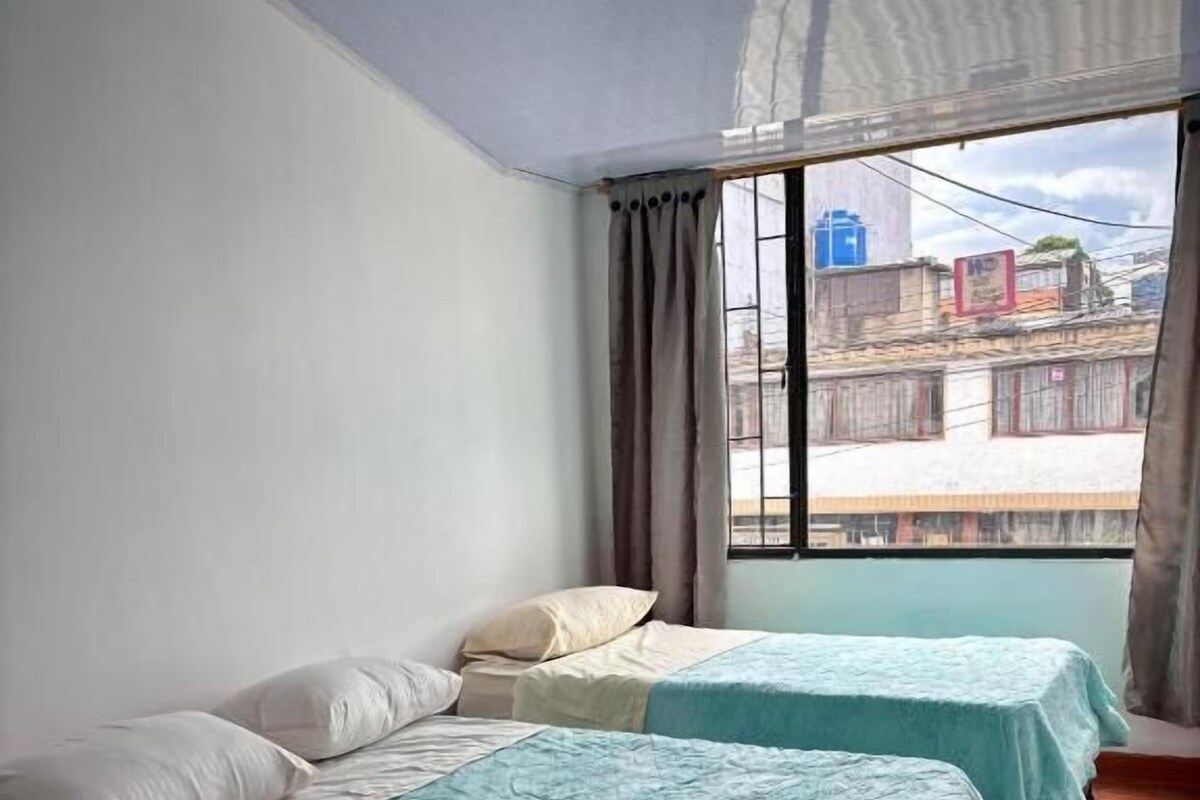 Une chambre avec deux lits, une fenêtre avec des rideaux et une vue sur les bâtiments environnants.
