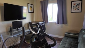 Un gimnasio en casa con una bicicleta estática, un televisor y un sofá.