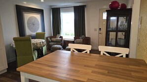 Un comedor con una mesa de madera, sillas verdes con diseño y un cuadro enmarcado, además de una puerta con paneles de vidrio.