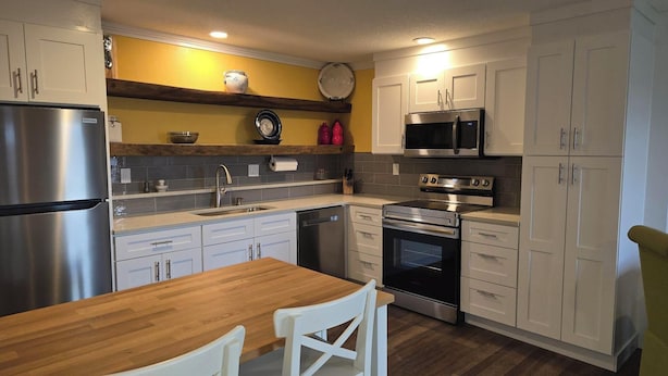 Una cocina moderna con electrodomésticos de acero inoxidable, una mesa de comedor de madera y armarios blancos.