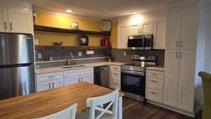 Una cocina moderna con electrodomésticos de acero inoxidable, una mesa de comedor de madera y armarios blancos.