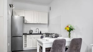 Una cocina compacta con armarios blancos, un refrigerador de acero inoxidable y un comedor con una mesa y dos sillas.