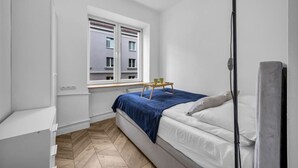 Un dormitorio con cama, mesita de noche, ventana y radiador.