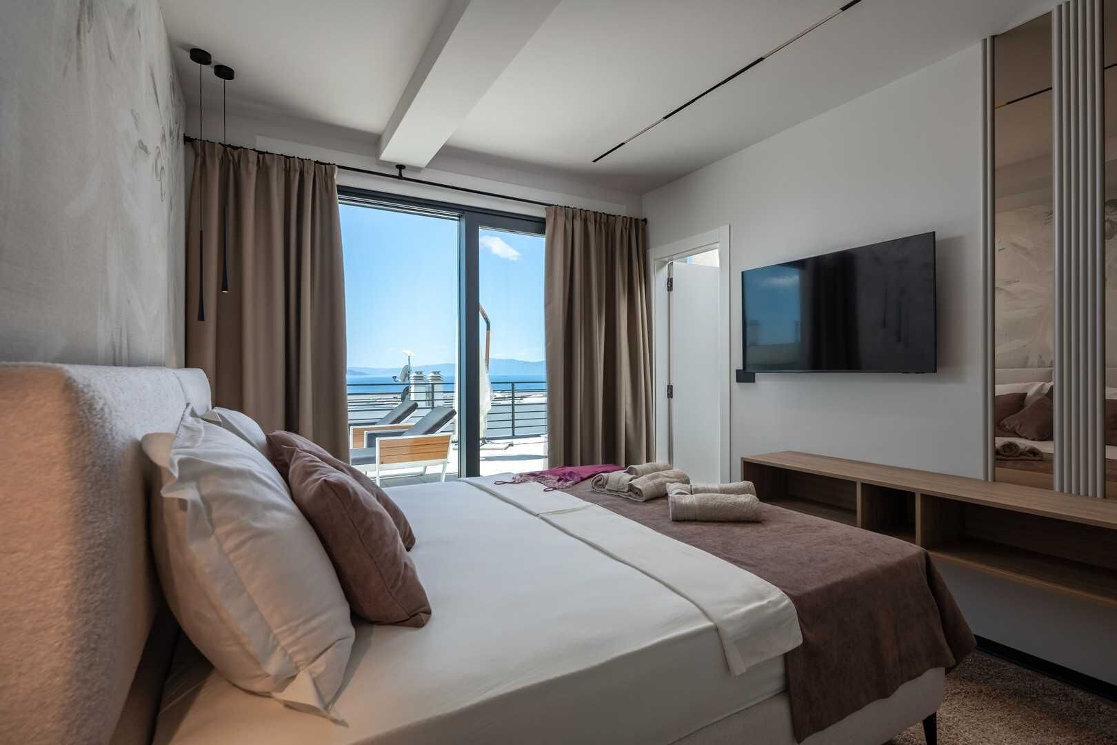 Ein Hotelzimmer mit Bett, Fernseher, Balkon mit Meerblick und einem Vorhangfenster.