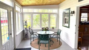 Una habitación luminosa con una mesa redonda y sillas, ventanas amplias y un cartel que dice 'Welcome'.
