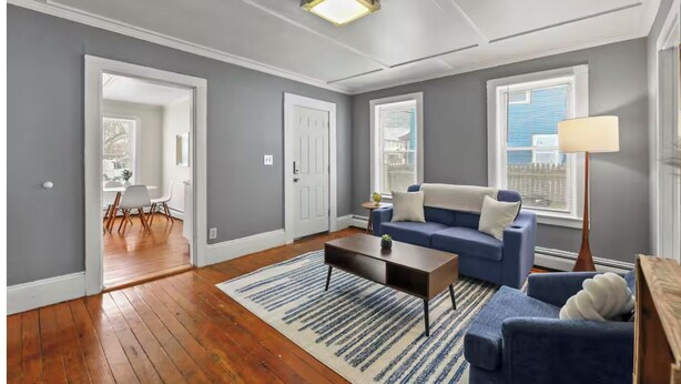 Un salón amplio con suelo de madera, un sofá azul, una mesa de centro y una lámpara.