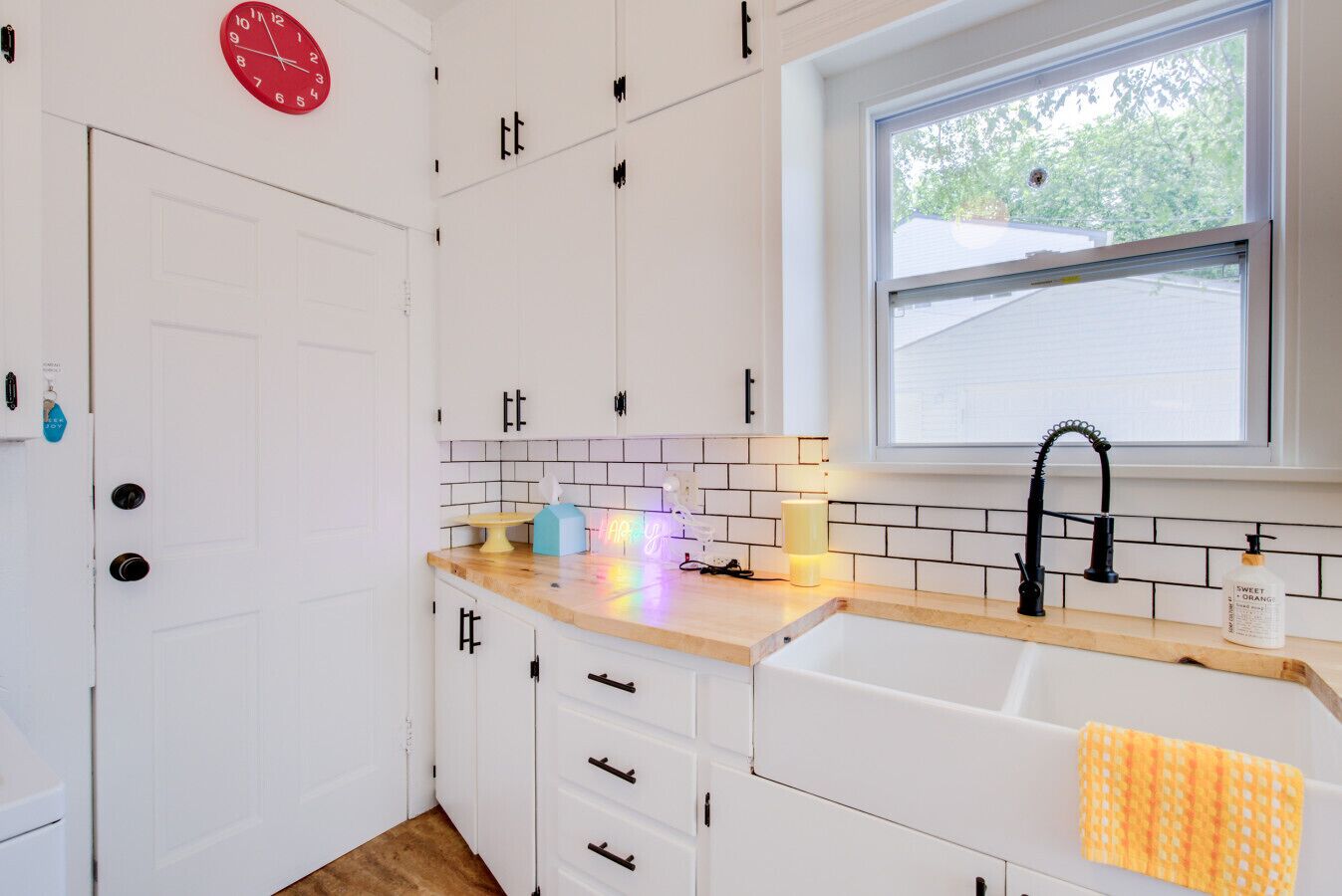 A kitchen with white cabinets, a wooden countertop, a sink, and a window with a view of the outside.