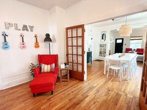 Une pièce avec une chaise rouge, une porte en bois, une table blanche et un mur orné de lettres en forme de guitare.