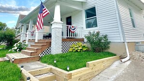 Una casa de dos pisos con un porche, una bandera y un pequeño jardín.