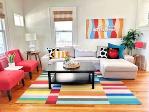 Ein Wohnzimmer mit einer Couch, Sesseln, einem Couchtisch und einem bunten Streifen Teppich.