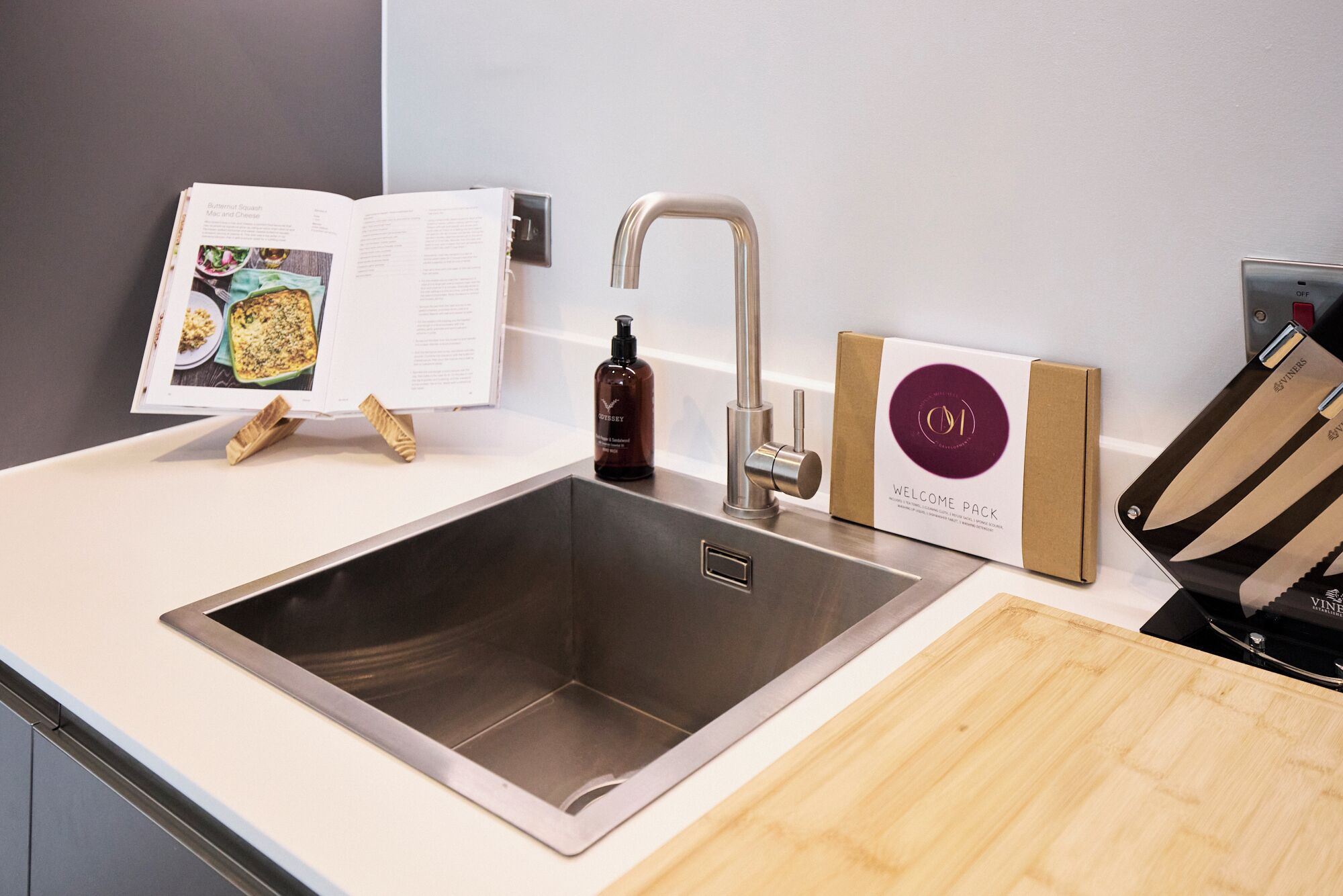 Une cuisine moderne équipée d’un évier en acier inoxydable, d’un livre de recettes, d’une bouteille d’huile d’olive et d’un kit d’accueil.