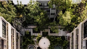 Un immeuble résidentiel à plusieurs étages doté d’une cour intérieure où se trouve une fontaine décorative, le tout entouré de balcons ornés de verdure.